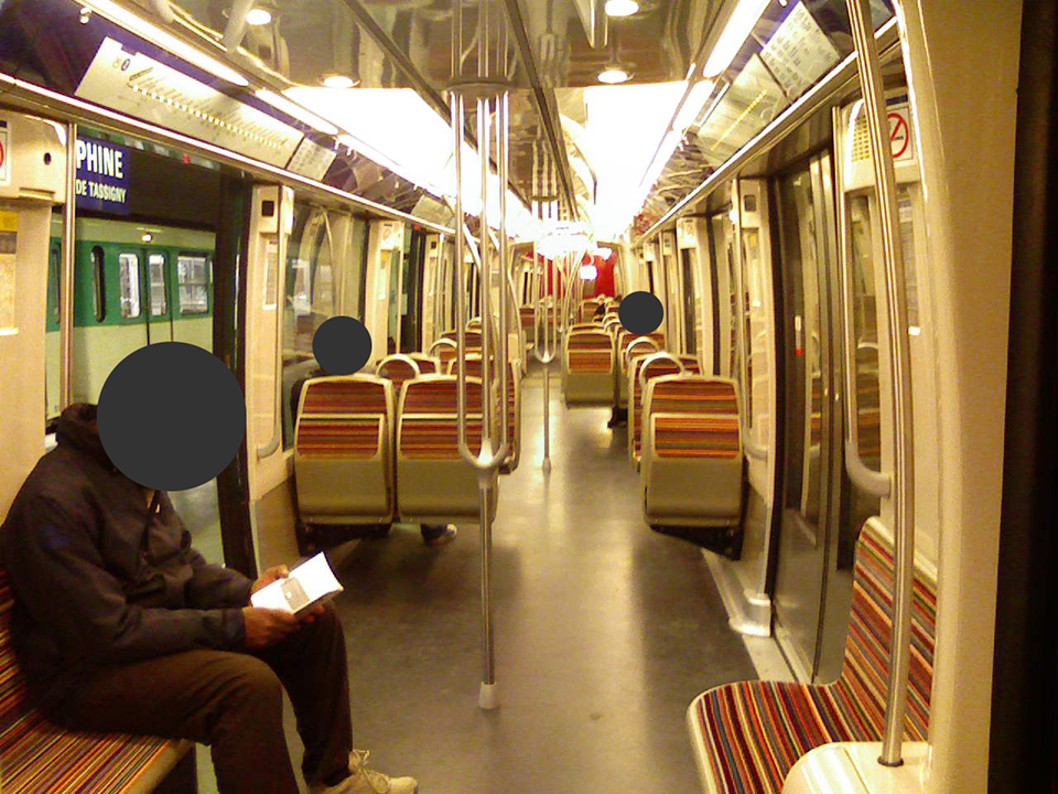 Photograph of the interior of a train of the line 2 of the Paris metro, featuring three people (of whom the faces have been censored with black circles for anonymity).